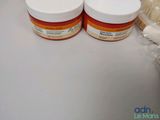 two jars of cream sitting on a counter next to a brush