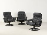 trois fauteuils inclinables en cuir noir et un tabouret dans une pièce blanche