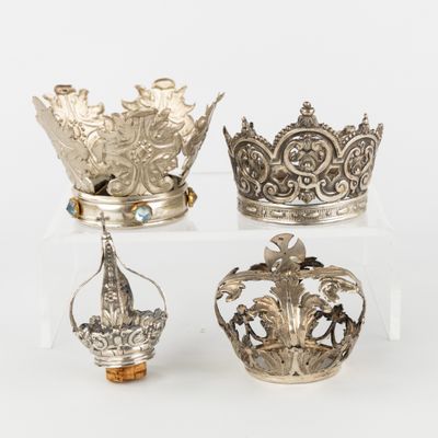 trois couronnes en argent sont posées sur un socle transparent, sur une surface blanche