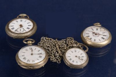 Trois montres de poche anciennes sont posées sur une table, reliées entre elles par une chaîne.