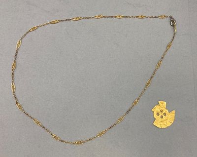 un collier en or et une pièce d'or posés sur une surface grise
