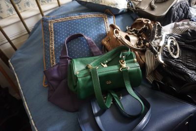 de nombreux sacs et sacs à main posés sur un lit, avec une chaise en arrière-plan