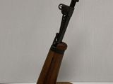 un fusil posé sur un support en bois, sur une surface blanche