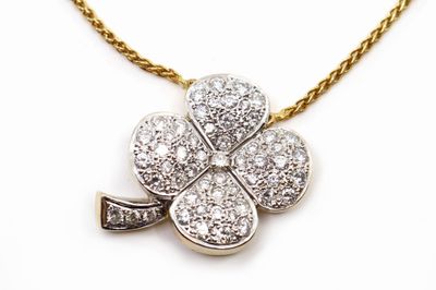 un gros plan d'un pendentif en forme de trèfle serti de diamants, monté sur une chaîne en or