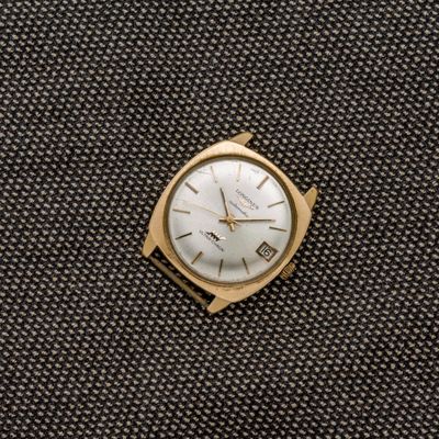 une montre en or posée sur un tissu noir, avec un cadran blanc