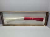 a red and white brush in a wooden frame on a white surface