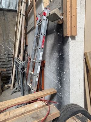 une échelle appuyée contre un mur, à côté d'un tas de bois