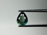 un gros plan sur une tourmaline verte tenue par une paire de pinces