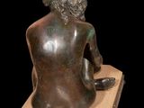 statue of a woman sitting on a stone block with her back to the camera