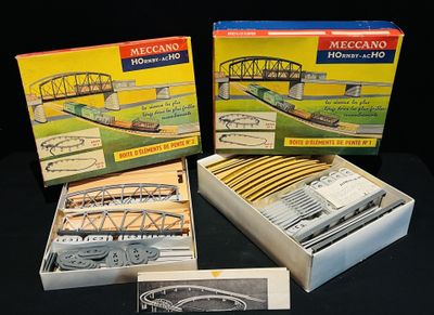 trois trains miniatures dans leurs boîtes, posés sur une surface noire, avec un pont en arrière-plan