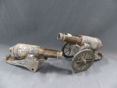 paire de canons anciens plaqués argent, munis de roues en bois, sur fond gris