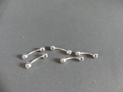 two pairs of silver nose piercings on a gray surface
