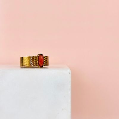 l'image d'une bague en or sertie d'une pierre rouge, posée sur un bloc