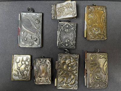 six étuis à cigarettes anciens en argent et en or sont alignés sur une surface noire