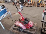 une petite tondeuse rouge posée sur une palette dans un garage