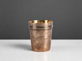 une petite tasse en cuivre posée sur une table blanche, sur fond gris