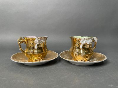 two cups and saucers decorated with gold and white flowers