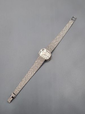 une montre argentée posée sur une surface grise, sur fond blanc
