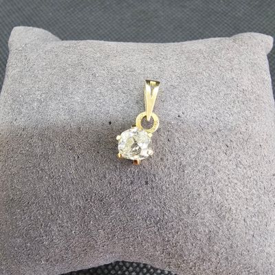 pendentif en or jaune serti d'un diamant, posé sur un coussin, sur fond gris