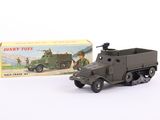 un camion de guerre miniature et une boîte posés sur une surface blanche, avec une autre boîte en arrière-plan
