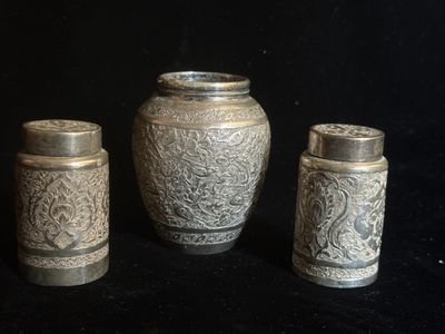 trois vases en argent posés les uns à côté des autres sur une surface noire