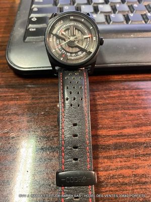 a watch sitting on top of a wooden table next to a laptop