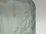 a green glass bottle with writing on it sitting on a table