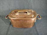 an old copper colored casserole with handles on a black background