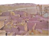 tableau représentant un village au milieu du désert, avec des montagnes en arrière-plan