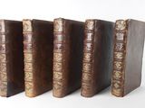 four old books are lined up in a row on a white surface