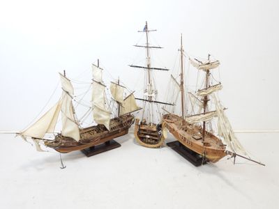 Deux maquettes de bateaux en bois avec des voiles sont exposées sur une surface blanche