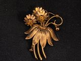 une photo d'une broche ornée de fleurs, posée sur un tissu noir