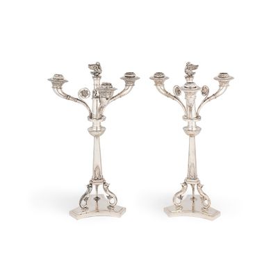 une paire de bougeoirs en argent posés sur des socles, sur fond blanc