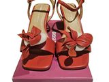 une paire de sandales rouges à talons hauts ornées d'un nœud, posée sur une boîte rose