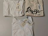 three white shirts with black writing on them sitting on a table