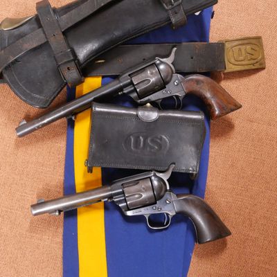 deux revolvers et un étui fixés à une ceinture rayée bleue et jaune