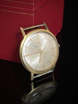 une montre en or posée sur une table noire, à côté d'une boîte rouge