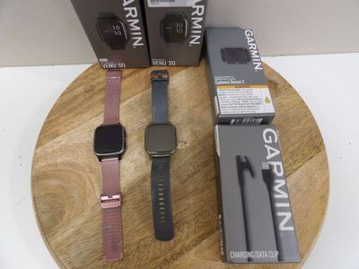 two watches on a wooden plate next to a box of garmin