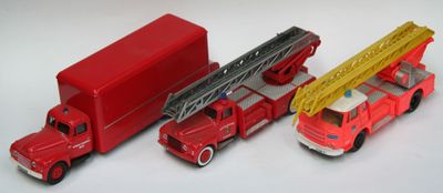 trois camions de pompiers miniatures et un camion posés sur une surface blanche