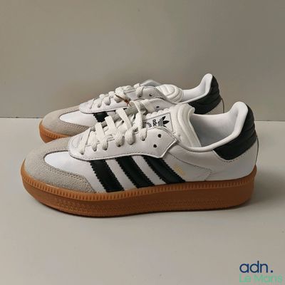 baskets adidas blanches et noires avec des semelles en caoutchouc sur une base blanche