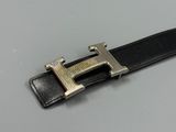 black leather belt with a silver buckle on a gray surface