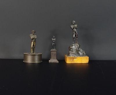 trois statues en bronze représentant un homme et une femme, posées sur un bloc de marbre