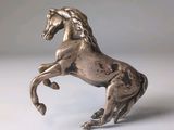 statue en argent représentant un cheval dressé sur ses pattes arrière, posée sur une surface blanche