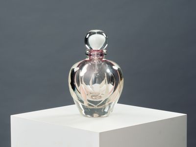 une bouteille en verre contenant une fleur, posée sur un socle blanc