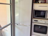 un réfrigérateur et un four dans une cuisine située à côté d'une porte-fenêtre coulissante