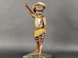 une statue en bronze représentant un garçon coiffé d'un chapeau, posée sur un socle en marbre
