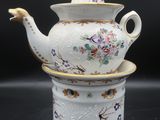 une théière blanche bordée d'or, sur laquelle est posée une tasse à thé