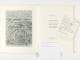 un livre ouvert sur lequel repose une feuille de papier, à côté d'une autre feuille sur laquelle sont inscrits des mots