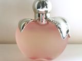 un flacon de parfum en verre rose avec un bouchon argenté, posé sur une surface blanche