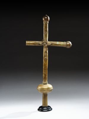 une croix dorée posée sur un socle noir, sur fond blanc